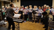 Die Sänger des Chorverein Kisdorf singen. Der Chorleiter steht am Klavier und dirigiert.  Foto: Marie Meyer