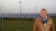 John Ingwersen aus Bosbüll steht vor Solaranlagen und Windrädern © NDR Foto: Sebastian Parzanny