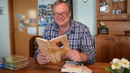 Carsten-Broder Feddersen sitzt am Tisch mit vielen Büchern © NDR Foto: Iris Guhl-Lengeling