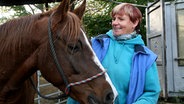 Reitlehrerin Claudia Fink-Cortum streichelt ein braunes Pferd. © NDR Foto: Nadine Dietrich