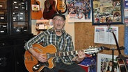 Brunsbütteler Klaus Keck spielt in einem mit Postern behangenen Zimmer, Gitarre und Mundharmonika und singt dazu © NDR Foto: Carsten Rauterberg