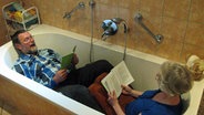 Dirk Mehlert-Gams liegt mit seiner Frau angekleidet in einer Badewanne und liest laut aus einem Buch © NDR Foto: Peter Bartelt
