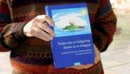 Jemand hält das Lexikon der friesischen Redewendungen "Twäärs üüs en haligschep" in den Händen. © NDR Foto: Karin Haug