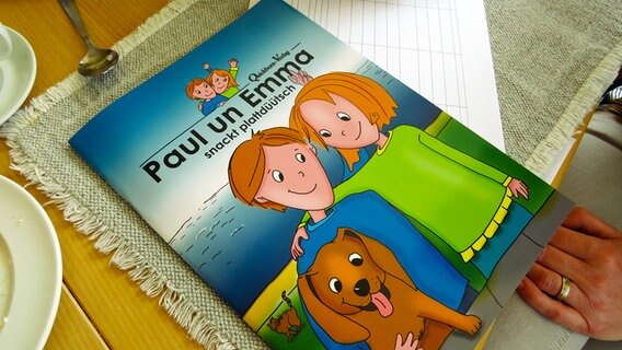 Auf einem Frühstückstisch liegt ein Plattdeutsches Kinderbuch. Auf einem Frühstückstisch liegt ein Plattdeutsches Kinderbuch. © NDR Foto: Karin Haug