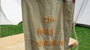 Eine Beutel mit dem Schriftzug "Ein paar Friesen" hängt vor einem Zelt. © NDR Foto: Karin Haug