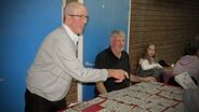 Hans Thomas, links im Bild, und Arnd Schaf verkaufen an einem Tisch Bingo-Karten. © NDR Foto: Karin Haug