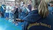 Eine Frau sitzt vor einer Gruppe singender Kinder © NDR Foto: Karin Hauug