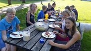 Zahlreiche Jugendliche sitzen bei einem gemütlichen Essen an einem Picknicktisch. © NDR Foto: Karin Haug
