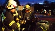 Zwei Feuerwehrmänner schneiden mit einer Rettungsschere die A-Säule eines Autos durch. © NDR Foto: Dana Frohbös