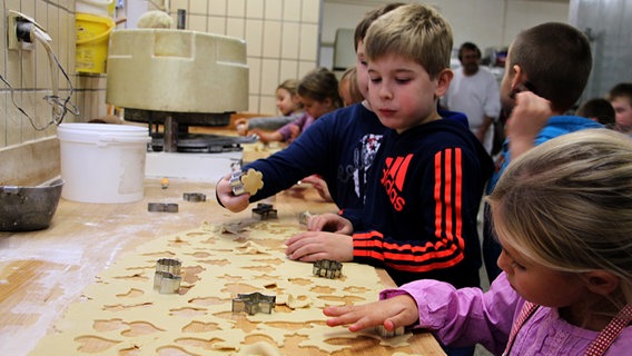 An einer langen Arbeitsfläche stechen Schüler Plätzchen aus Teig aus. © NDR Foto: Rebekka Merholz