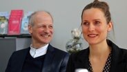 Ein Mann und eine Frau sitzen in einem Büro nebeneinander und schauen lächelnd in den Raum hinein. © NDR Foto: Lornz Lorenzen
