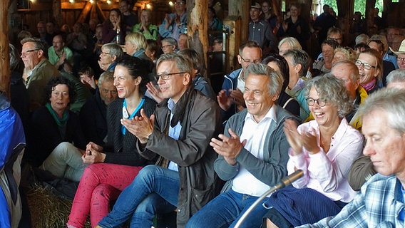 Zuschauer sitzen auf Strohballen in einer Scheune und applaudieren. © NDR Foto: Lornz Lorenzen