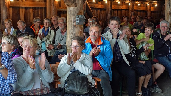 Zuschauer sitzen auf Strohballen in einer Scheune und applaudieren. © NDR Foto: Lornz Lorenzen