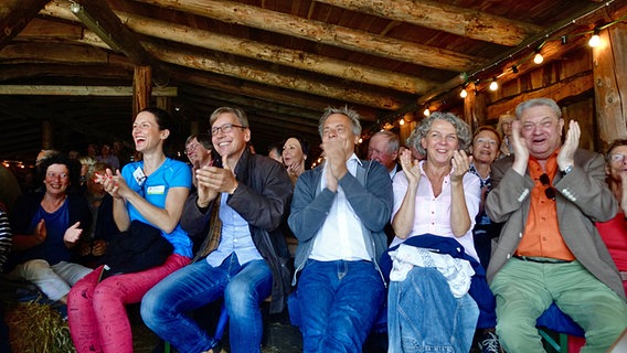 Zuschauer sitzen auf Strohballen in einer Scheune und applaudieren. © NDR Foto: Lornz Lorenzen