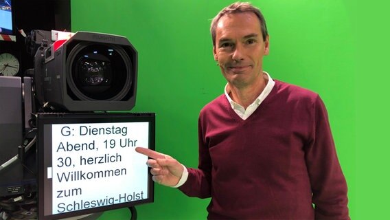 Meeno Schrader zeigt im Greenscreen-Studio auf den Telepromter. © NDR 