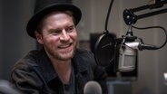 Johannes Oerding sitzt vor einem Mikrofon in einem Hörfunkstudio. © NDR Foto: Janis Röhlig