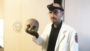 Dr. Mark Benecke hält einen Totenkopf in die Kamera. © NDR Foto: Jan Malte Andresen