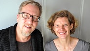 Eva Strehle und Jan Malte Andresen stehen gemeinsam vor einer weißen Wand im NDR 1 Welle Nord Sendestudio und lächeln in die Kamera. © NDR Foto: Samir Chawki