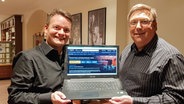 Schauspieler Christian Becker und Spielleiter und Schauspieler Jan Steffen zeigen einen Laptop in die Kamera. © NDR Foto: Janina Harder