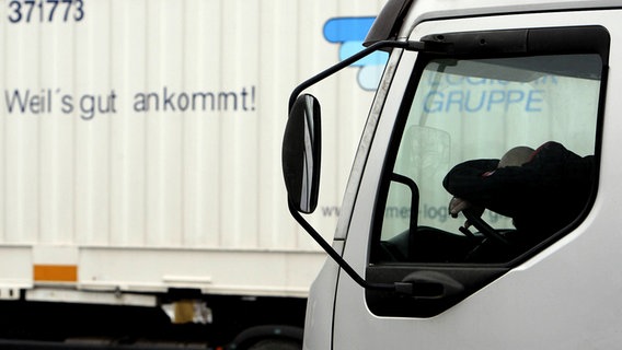 Ein Lkw-Fahrer hat seinen Kopf auf dem Lenkrad im Führerhaus eines Lkws abgelegt. © imago Foto: biky