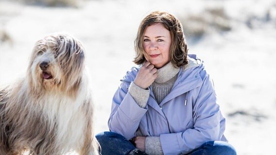 Elke Weiler sitzt mit einem Hund am Strand © Stine Jans Fotografie Foto: Stine Jans Fotografie