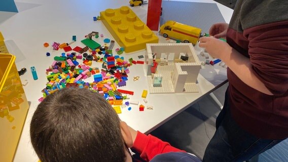 Zwei Jungs bauen Legosteine zusammen, die durcheinander und mit vielen bunten Steinen vor ihnen liegen. Zwei Jungs bauen Legosteine zusammen, die durcheinander und mit vielen bunten Steinen vor ihnen liegen. © NDR / Linda Ebener Foto: Linda Ebener
