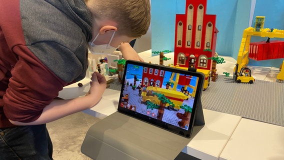 Jeremy setzt die Legofiguren in Szene und schaut, dass alle richtig stehen. Vorne ist ein Tablet aufgebaut, mit dem jede einzelne Szene fotografiert wird. © NDR / Linda Ebener Foto: Linda Ebener
