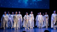 Kinder und Jugendliche mit silbernen Umhängen stehen auf einer Theaterbühne. © NDR Foto: Thomas Lorenzen