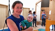 Kirsten Jacobsen lächelt mit einem Baby auf dem Arm in die Kamera. © NDR Foto: Peer-Axel Kroesle