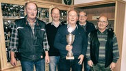 Karl-Heinz Sohn steht mit einem Pokal in der Hand zwischen vier weiteren Männern und in einem Schrank im Hintergrund stehen noch mehr Pokale. © NDR Foto: Ines Barber