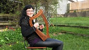 Eine junge Frau sitzt im Garten auf einem Stuhl und spielt Harfe. © NDR Foto: Stephanie Bommes Alvarez