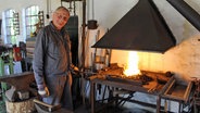 Heinrich Stark steht vor einem Schmiedeofen. © NDR Foto: Andrea Ring