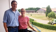 Imke und Markus Riessen stehen auf einem Balkon. Im Hintergrund befindet sich ein Bauernhof. © NDR Foto: Iris Guhl