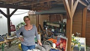 Heike Kschioneck steht unter einem Carport mit Flohmarktrödel und lächelt in die Kamera. © NDR Foto: Frank Hajasch