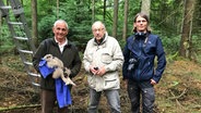 Hans-Wilhelm Hansen mit junger Eule im Arm, Karl-Heinz Reiser und Felix Hansen stehen im Wald. © NDR Foto: Nils Hansen