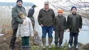 Christoph Keller (Mitte) mit Kindern der Jugendgruppe und seinem Freund und Mitstreiter, Förster Thorolf Wellmer direkt am See vor einer Holz-Adler-Figur. © NDR Foto: Ines Barber