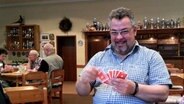 Hans-Peter Guhlke sitzt in einer Gaststätte und spielt Karten. © NDR Foto: Jörn Schaar