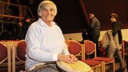Rita Frank sitzt in einer Stuhlreihe und hat ihre Hände auf eine Trommel gelegt. © NDR Foto: Tobias Senff