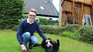 Ein junger Mann mit Brille hockt auf dem Rasen und streichelt einen Hund der neben ihm auf dem Rücken liegt. © NDR Foto: Tobias Senff