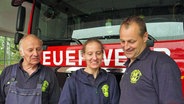 Nadina Lattka steht zwischen ihrem Vater Uwe (l.) und Sven Johansson vor einem Feuerwehr-Einsatzfahrzeug und schaut auf einen Zettel in ihrer Hand. © NDR Foto: Frank Hajasch