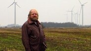 Reinhard Christiansen aus Ellhöft steht auf einem Feld mit Winkrafträdern im Hintergrund © NDR Foto: Peer-Axel Kroeske