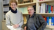 ( v.l.n.r.) Robert Langhanke, wissenschaftlicher Mitarbeiter in der Niederdeutsch-Abteilung des Germanistischen Seminars und Prof. Dr. Michael Elmentaler stehen vor einem Bücherregal © NDR Foto: Ines Barber