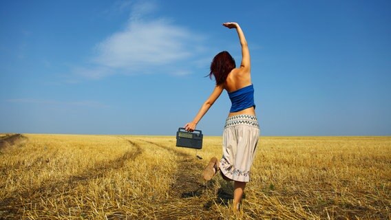 Frau tanzt mit einem Radio über ein Stoppelfeld. © Masson / fotolia Foto: Masson
