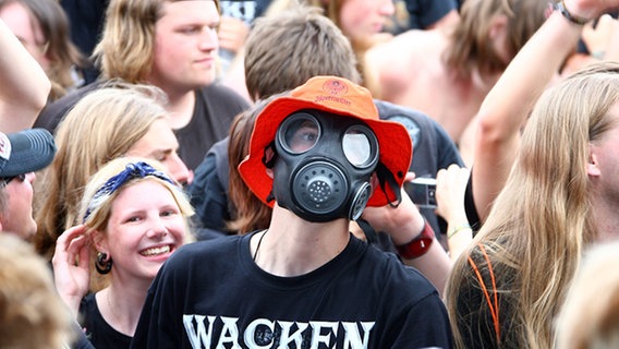 Ein Fan verfolgt den Auftritt der Feuerwehrkapelle Firefighters mit einer aufgesetzten Gasmaske © dpa - Bildfunk Foto: Carsten Rehder