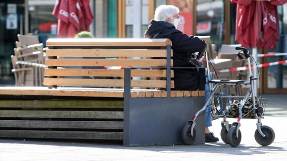 Eine Seniorin mit Mundschutz sitzt in Wolfsburg neben ihrem Rollator auf einer Bank. © imago images/Jan Huebner 