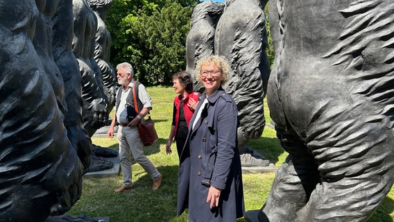 Julia Westlake steht neben Menschen in einer Affenskulpturengruppe und lacht in die Kamera. © NDR Foto: Hauke Sievers
