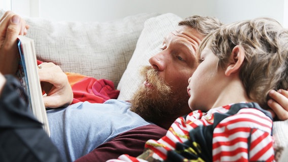 Ein Vater liest seinem Kind liegend auf dem Sofa vor. © photocase Foto: behrchen