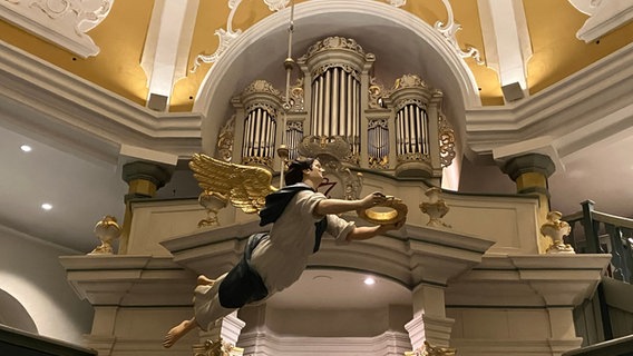 Ein Engel schwebt im Innenraum einer Kirch vor weißen Orgelpfeifen © NDR Franziska Storch Foto: Franziska Storch
