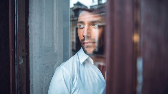 Ein junger Mann blickt durch eine Fensterscheibe nach draußen. © photocase.de Foto: klublu