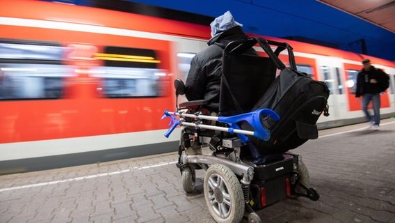 Eine im Rollstuhl sitzende Person am Bahngleis. Vor ihr fährt ein Zug. © picture alliance/dpa Foto: Marijan Murat